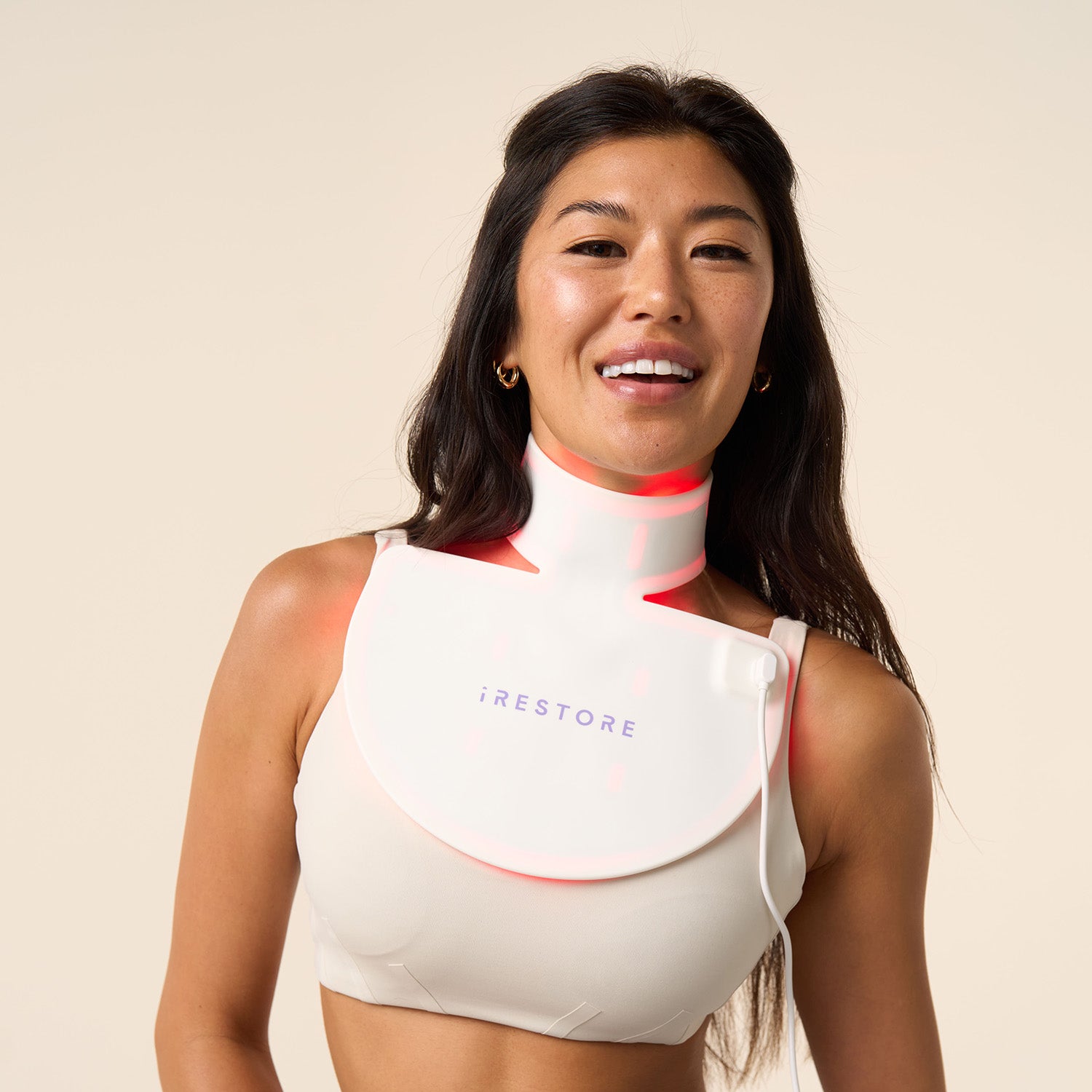 Woman smiling while wearing the iRESTORE LED neck and chest mask, with the red LED light turned on