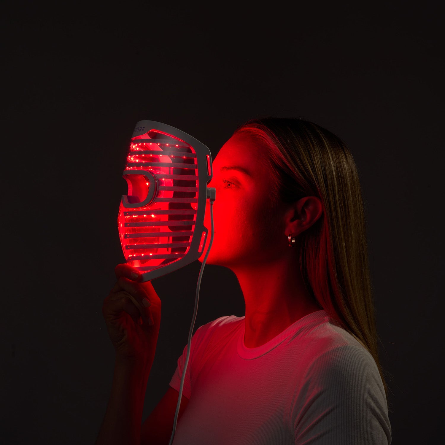 Woman holding the glowing red iRESTORE LED face mask in front of her face