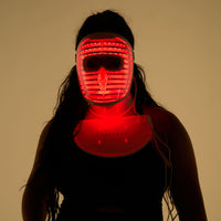 Silhouette of a woman wearing both the LED face mask and LED neck and chest mask with red light turned on with magsafe chargers attached to each device