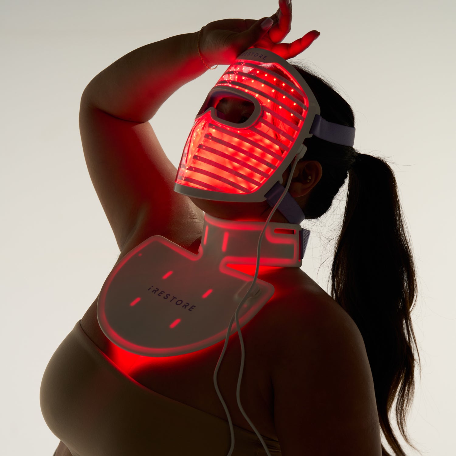 Silhouette of a woman wearing both the LED face mask and LED neck and chest mask with red light turned on