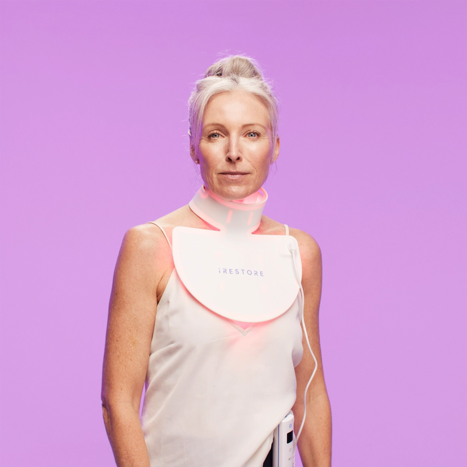 Mature woman on purple backgorund wearing the iRESTORE led neck and chest mask